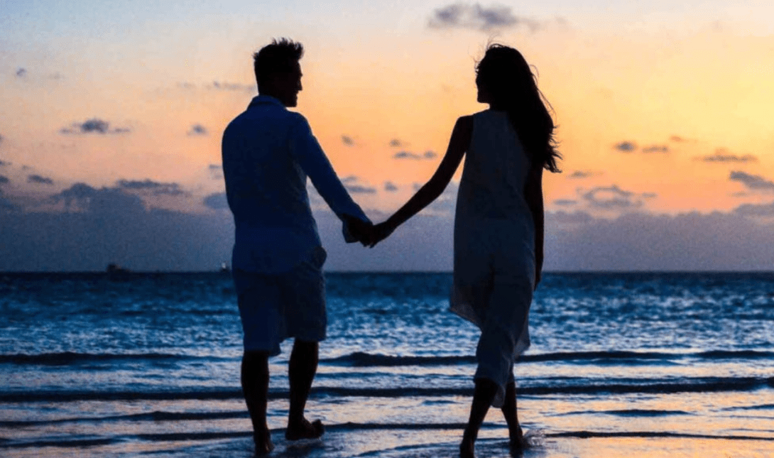 ζευγάρι περπατάει χέρι χέρι στη θάλασσα στο ηλιοβασίλεμα